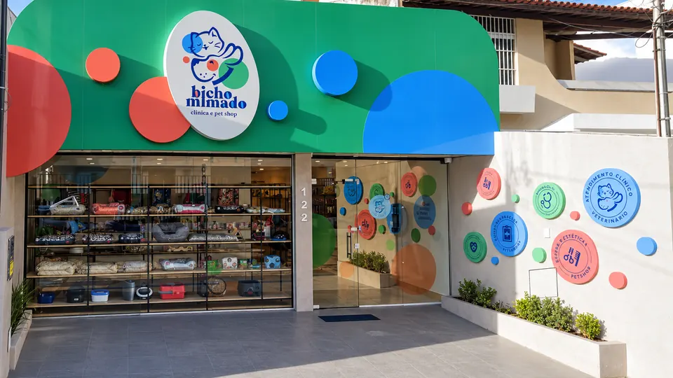 Fachada da Bicho Mimado: toldo verde com círculos coloridos e a placa oval com o logo, imagem tratada a partir da fachada real